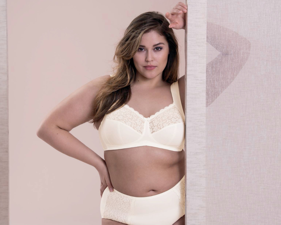 A woman standing next to a sheer curtain, wearing the Anita since 1886 Havanna wireless support bra and panty in color crystal