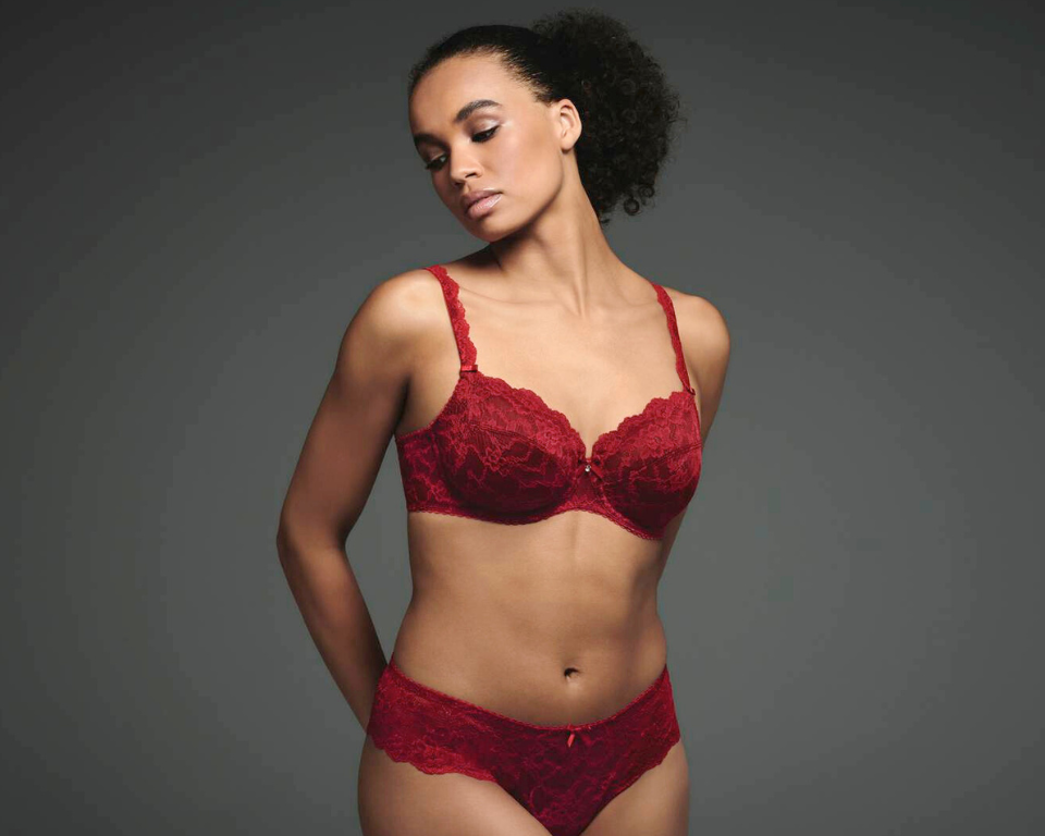 A standing woman wearing the Rosa Faia Bobette underwire bra and shorty in color rubin red.